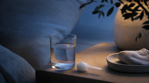 Editorial image of a glass of water and measured glycine powder on a bedside table in soft evening light, symbolizing simple sleep support and recovery.