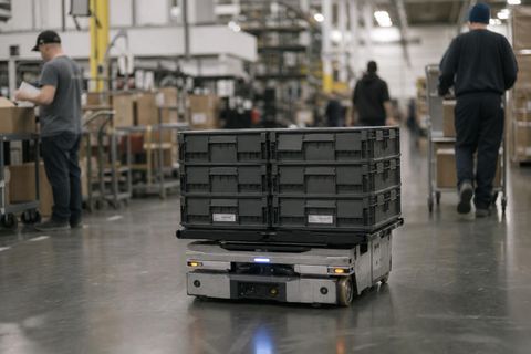Editorial image of a robot operating in a real mixed human work environment, symbolizing the gradual arrival of robots into everyday systems and society.
