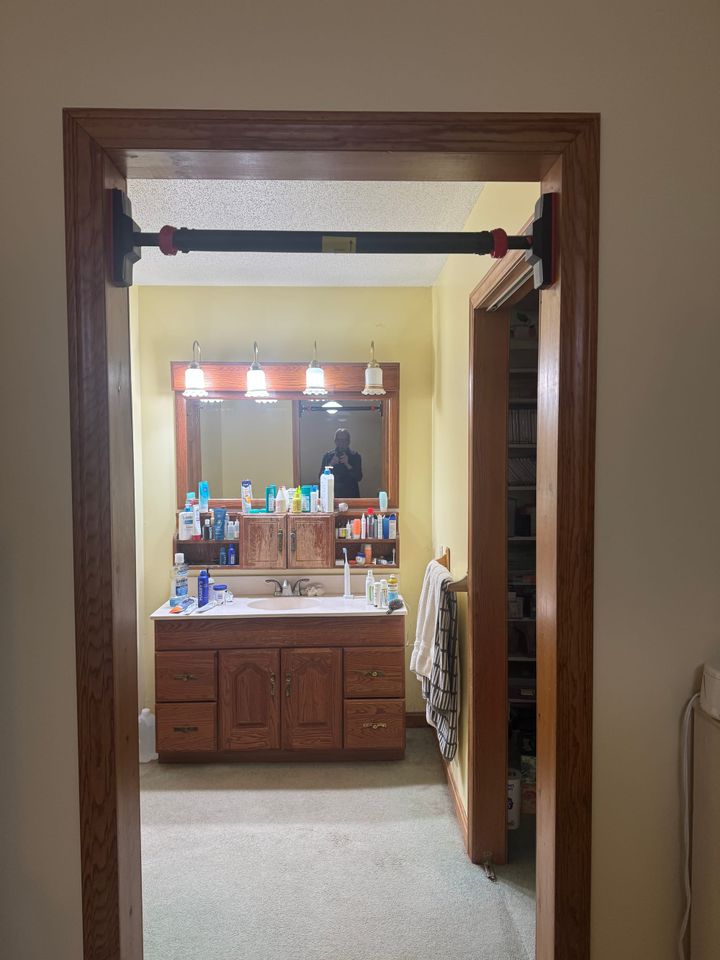 Pull-up bar mounted in a doorway, reflected in a bathroom mirror with the photographer visible in the reflection.