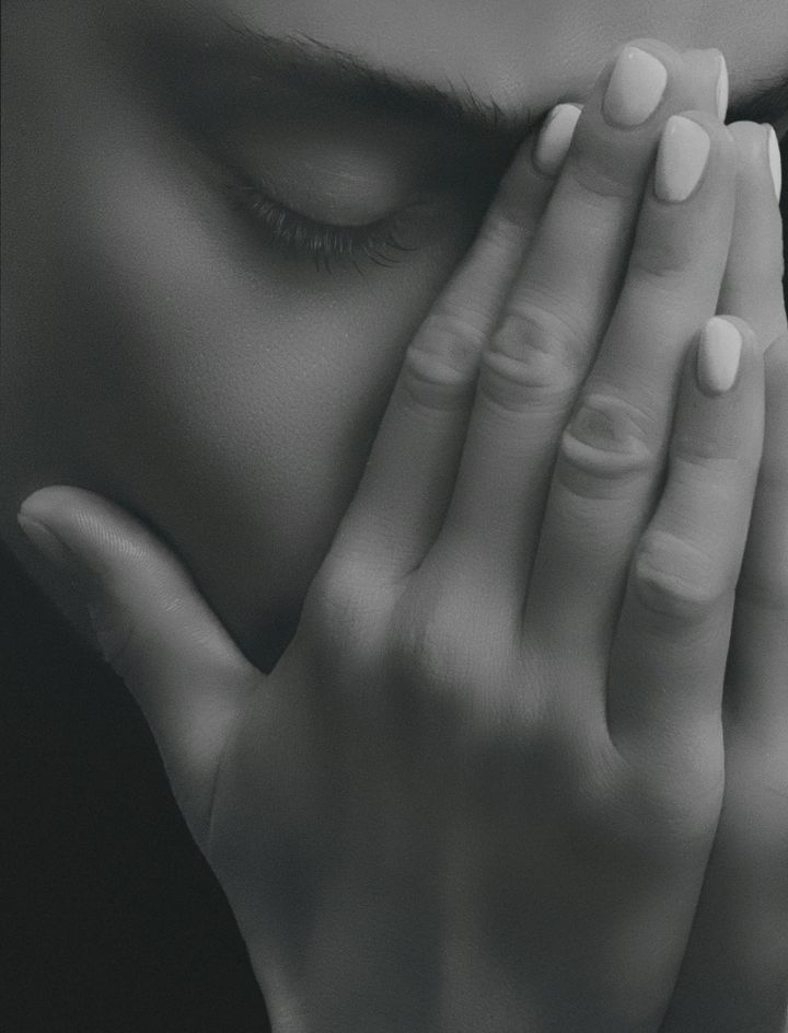 Close-up of a woman with her eyes closed, her hand covering part of her face.