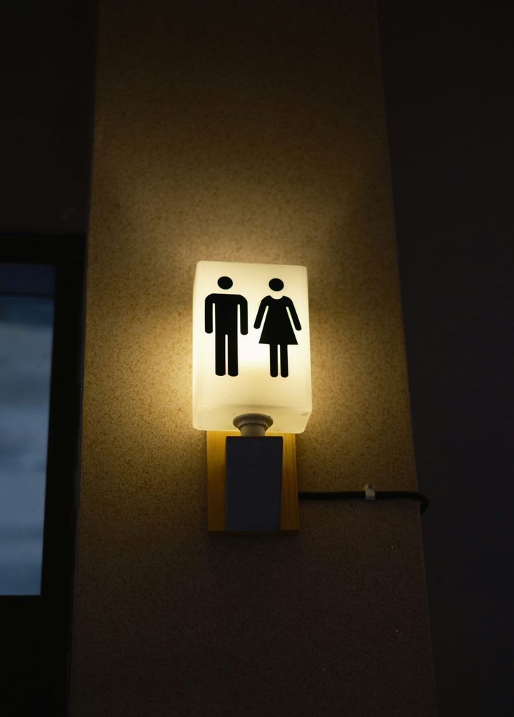 Illuminated restroom sign showing male and female figures glowing against a dark wall.