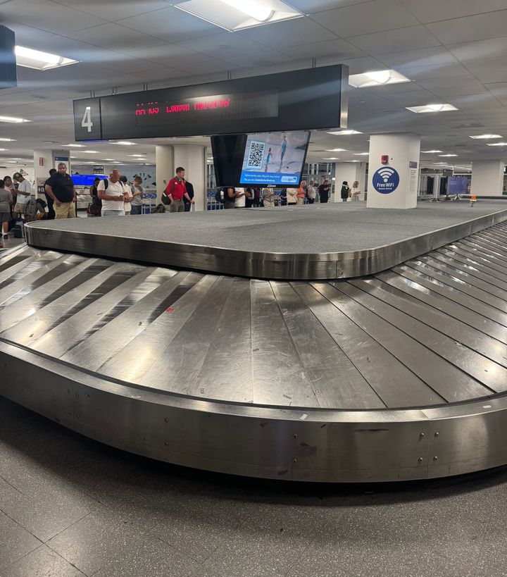 People waiting for their baggage next to an empty airport conveyor belt. 
