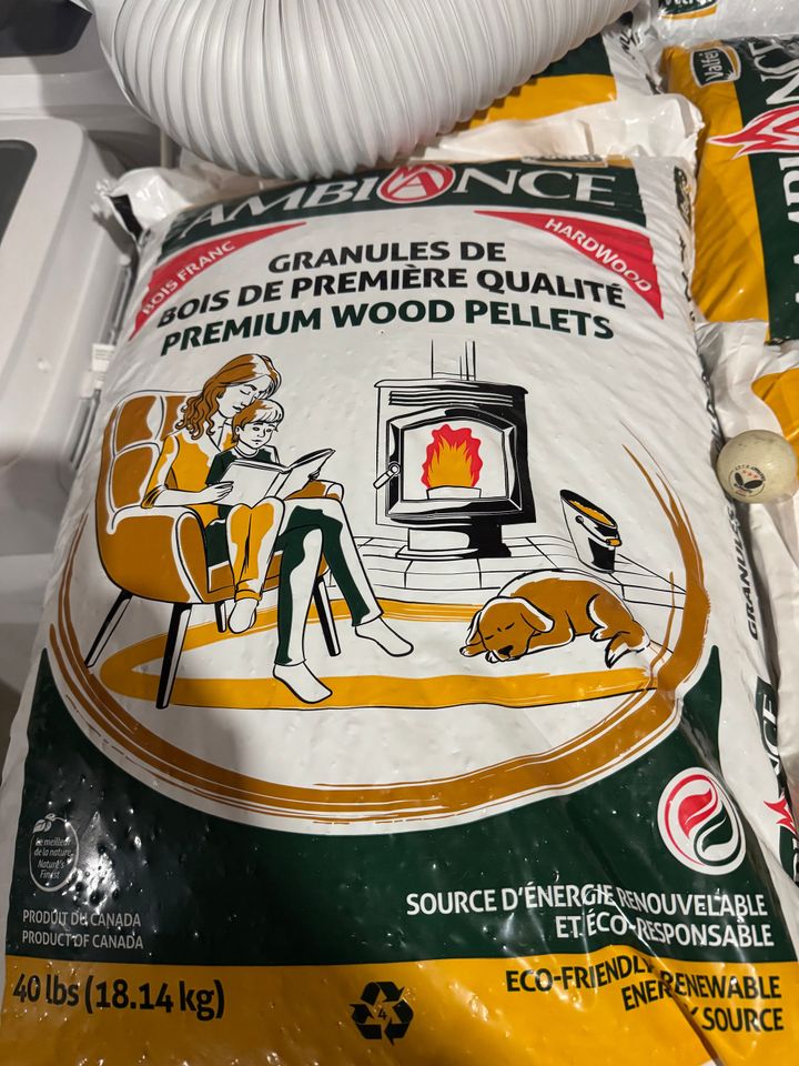 A bag of Ambiance wood pellets showing a family reading beside a warm stove, with a small ping-pong ball partly hidden at the right edge.