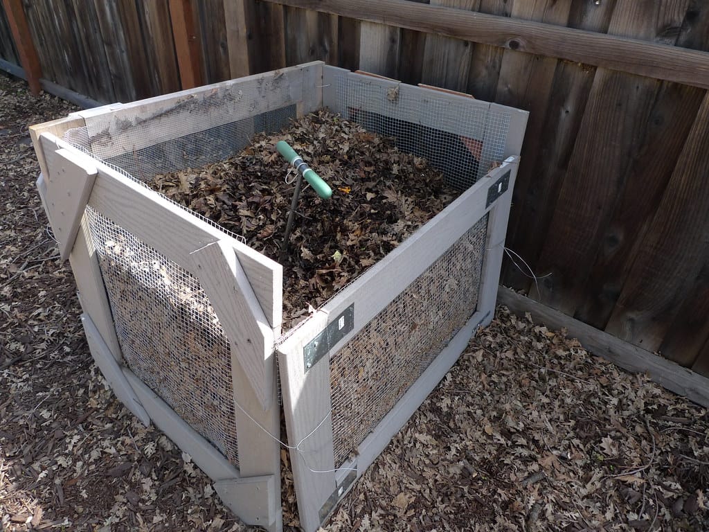 Backyard compost bin full of yard waste with a turning tool