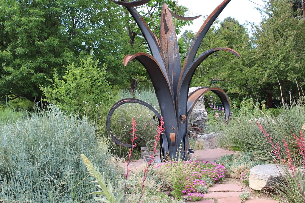 Lushly planted xeriscape garden with silver artemisia, red penstemon wands, pink groundcover and a flagstone path