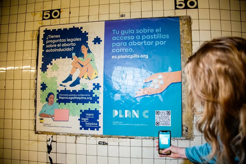 A woman scanning a QR code on her phone on an advertisement for Plan C pills.