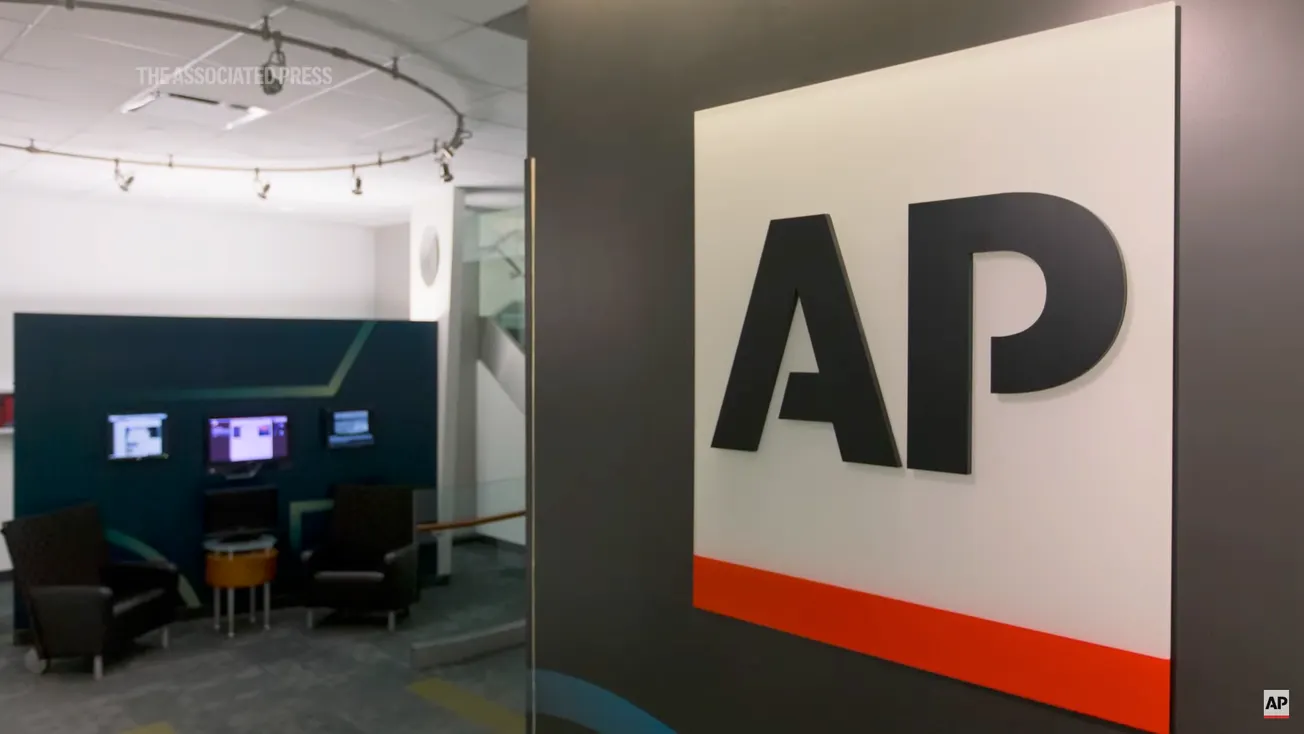 Interior of Associated Press offices including a black wall with the AP logo.