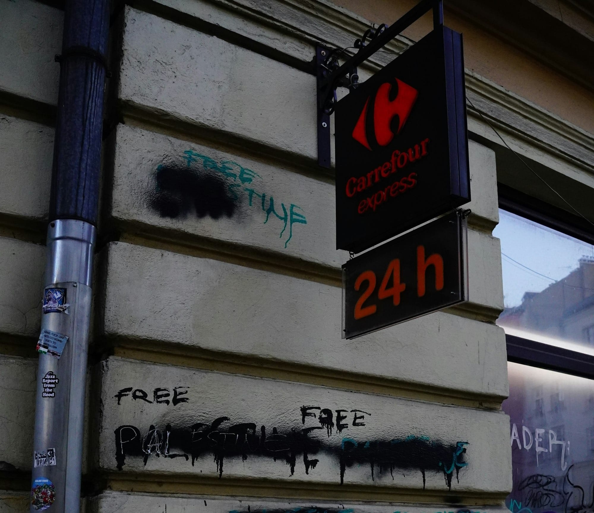 A Carrefour Express sign above a building wall covered in black spray-painted graffiti