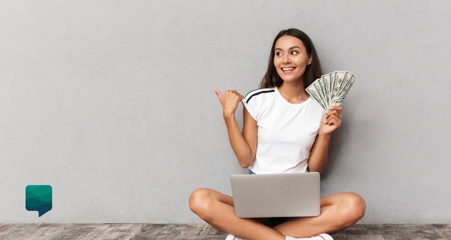 Quanto cobrar por aula particular de inglês? Professora com um computador no colo e dinheiro na mão.