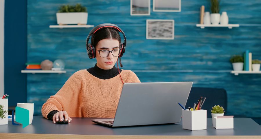 Foto de uma mulher em frente ao notebook usando fones de ouvidos. Como dar aula à distância.