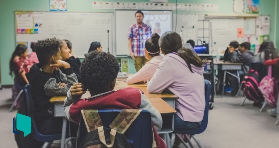 Rotação por estações (foto: alunos sentados em grupos em uma sala de aula com professor a frente explicando)