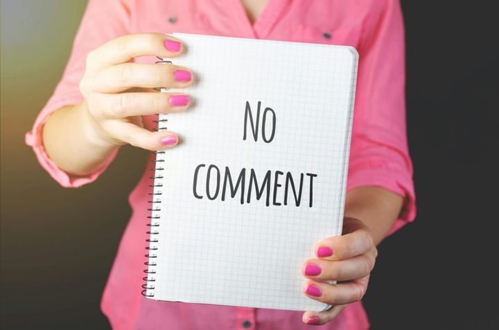 A woman in a pink shirt holds a notebook with 'No comment' text visible, conveying silence or privacy.