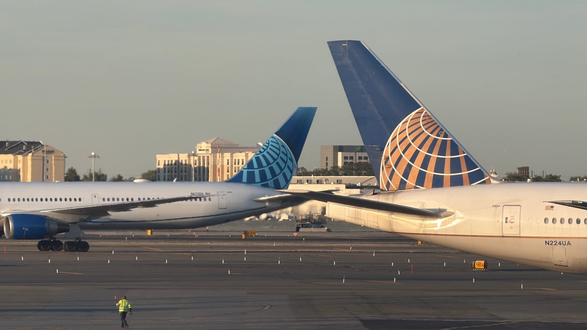 Two United Airlines widebody jets on the tarmac at Newark airport, with a ground worker walking nearby