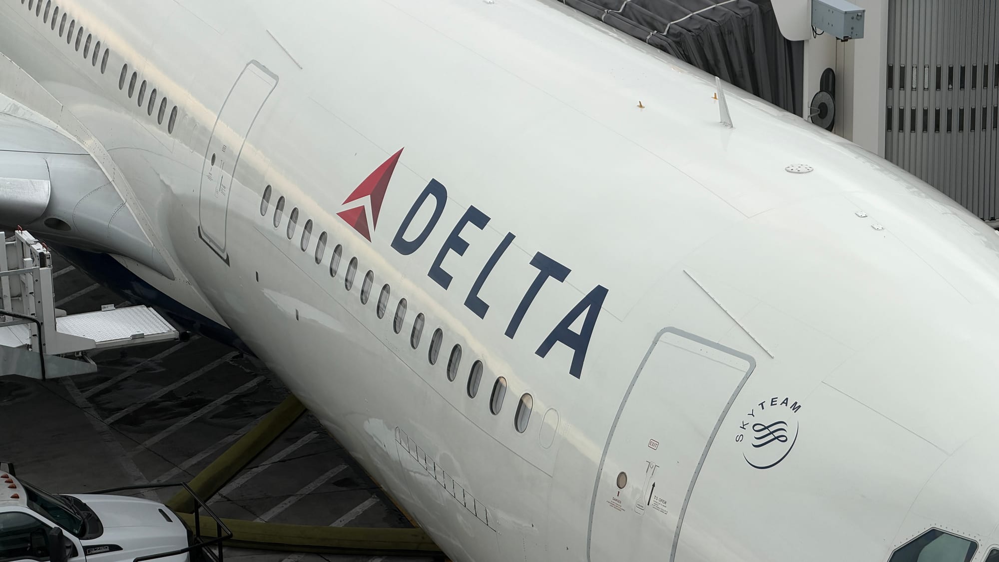 Side of a Delta jet parked at a gate, with its jet bridge and SkyTeam logo visible