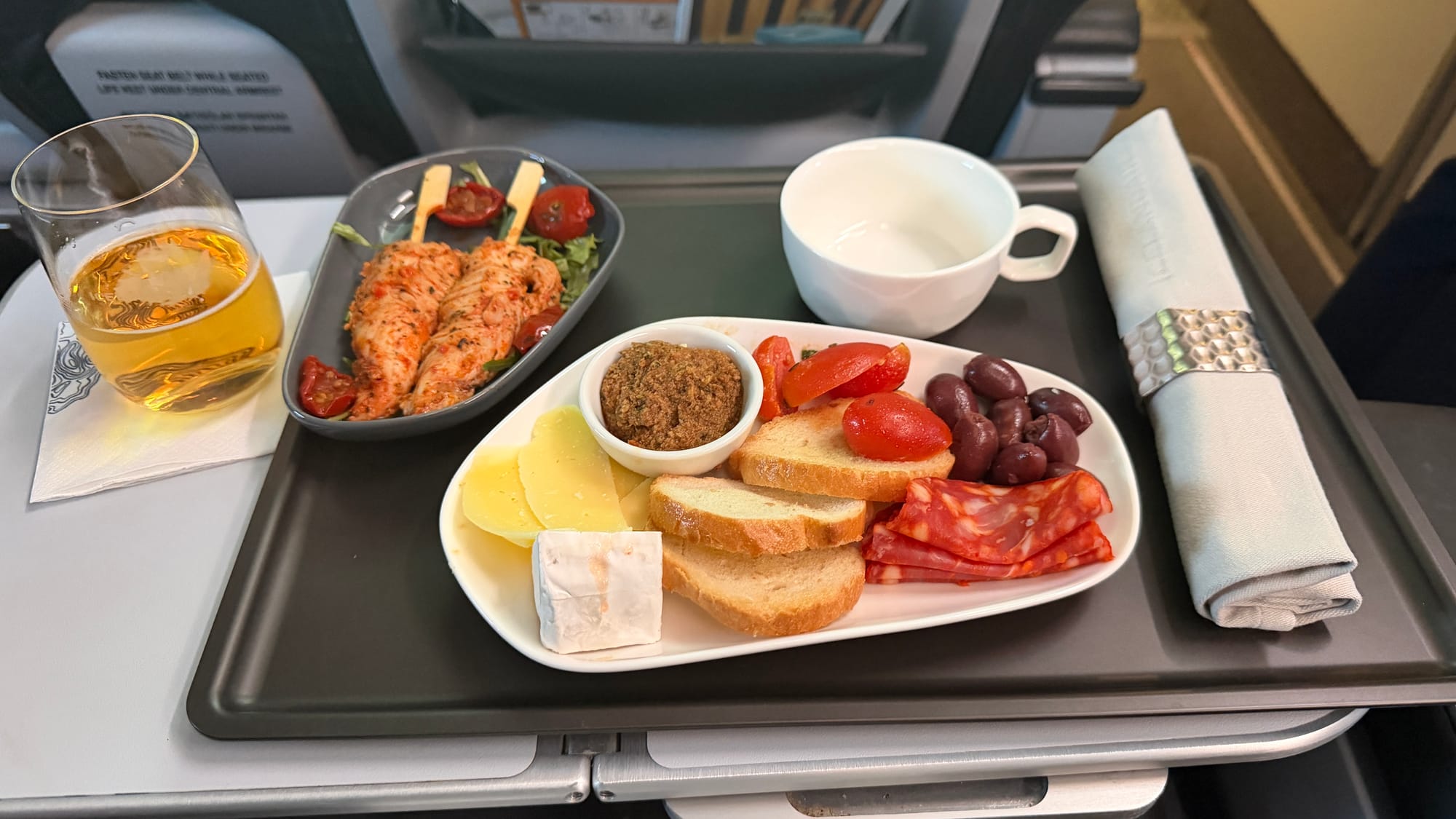 Icelandair business class meal tray with chicken skewers, bread, cheese, cured meats, olives, tomatoes and a glass of beer