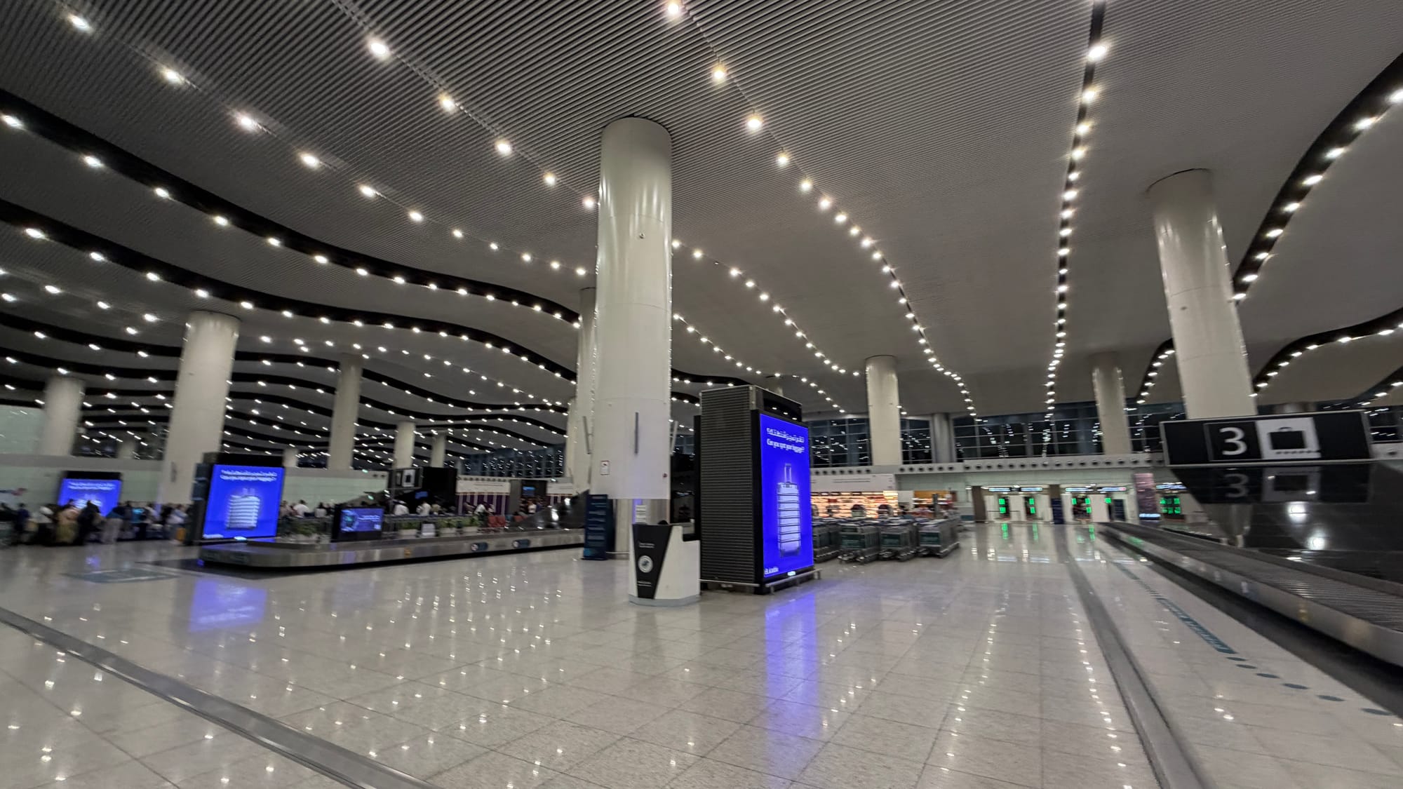 Large, brightly lit baggage claim hall at Riyadh’s King Khalid International Airport with white columns and carousels