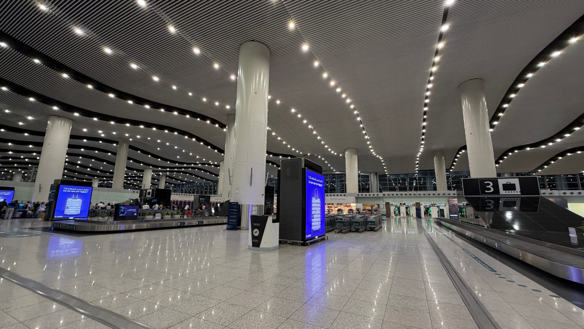 Bright baggage claim hall with white columns and a curved, lit ceiling at King Khalid International Airport in Riyadh