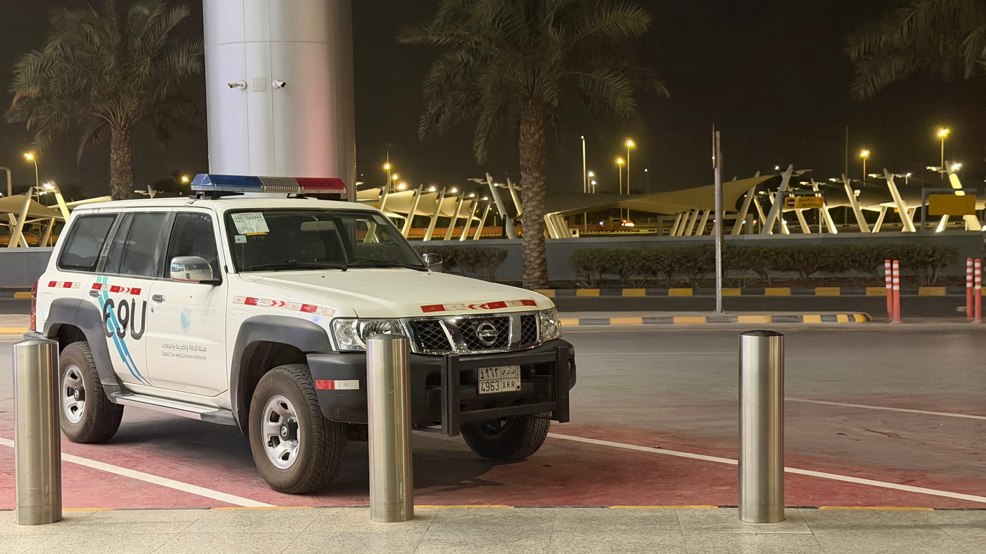 White Saudi security SUV with a light bar parked outside a terminal at King Khalid International Airport at night