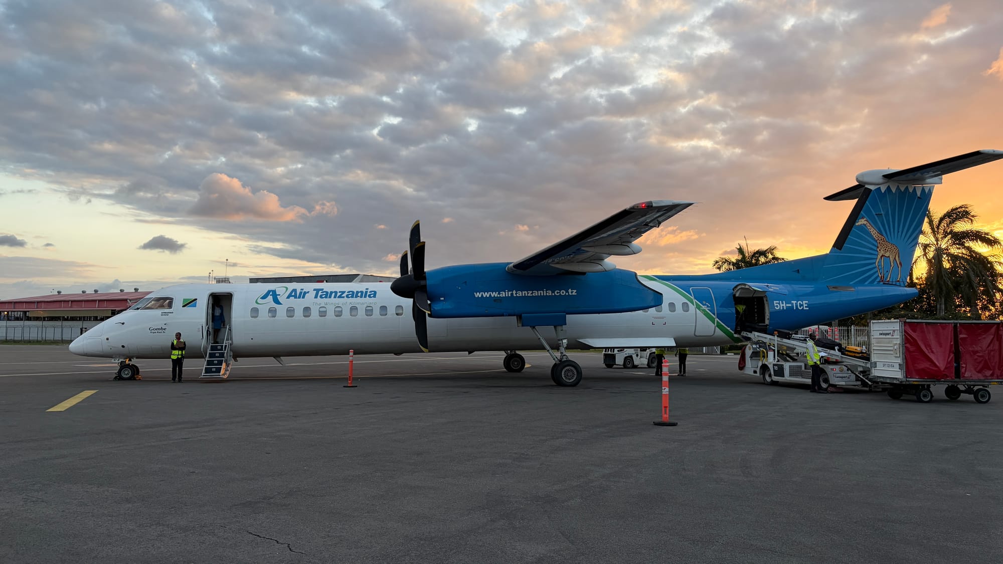 Air Tanzania Dash 8-400 propeller plane with a giraffe on its blue tail, parked on the tarmac at sunset in Dar es Salaam