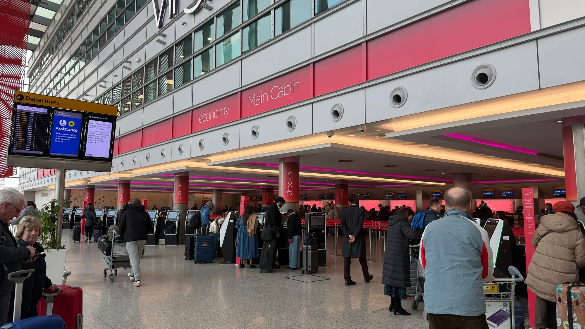 Travelers with luggage lining up at the Virgin Atlantic and Delta check-in counters inside Heathrow Terminal 3