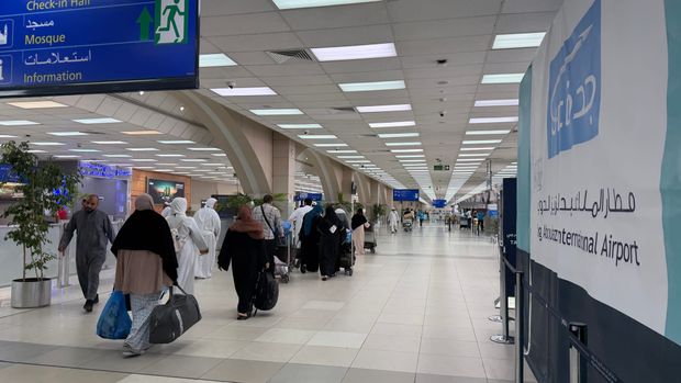 Travelers and pilgrims in white walking with luggage through a terminal hall at King Abdulaziz International Airport in Jeddah