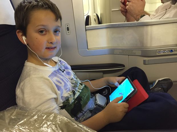 Young boy playing on a iPad in a British Airways Club World seat, with the privacy divider behind him