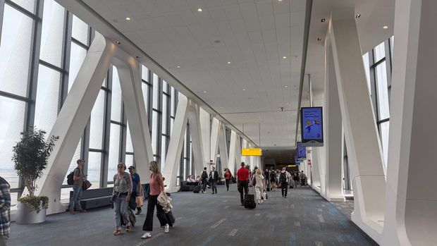 Travelers walking through a bright LaGuardia Airport concourse with tall windows and white angled columns