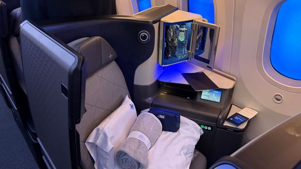 United Polaris business class seat with a privacy door, pillow, blanket and amenity kit beside a dimmed 787 window