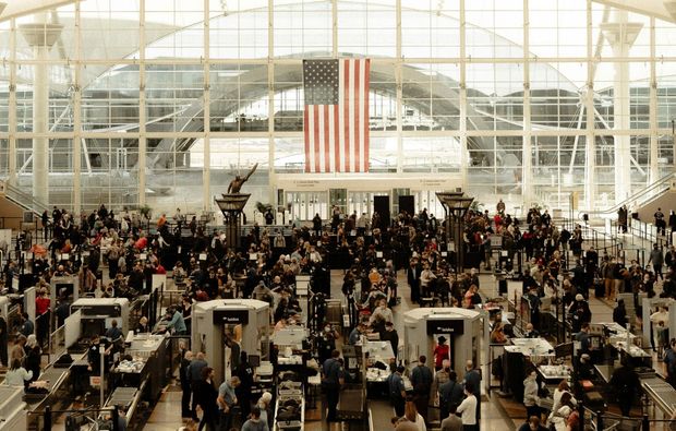 Crowded security checkpoint inside Denver International Airport’s terminal with a large American flag hanging overhead