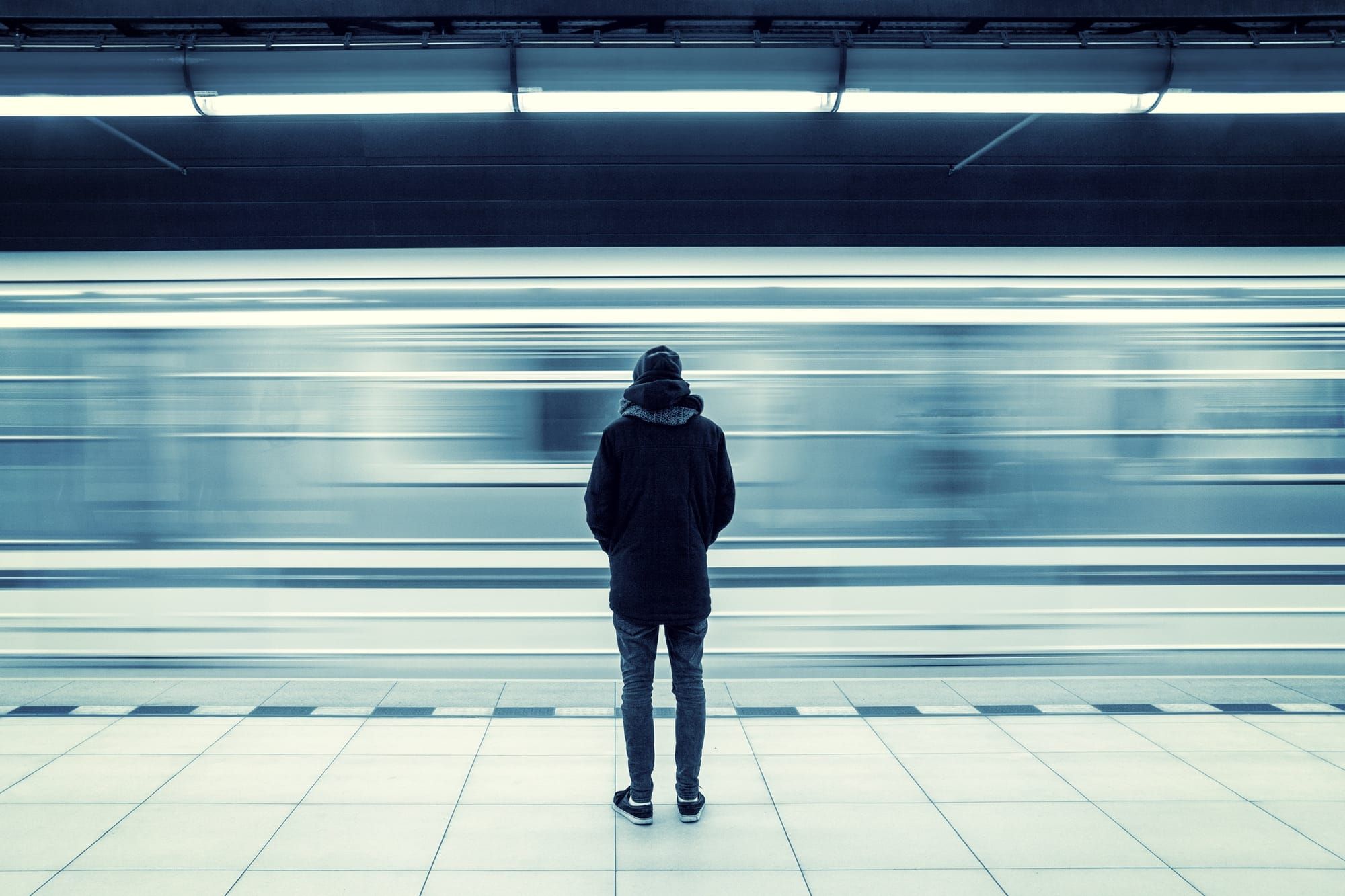 A solitary figure waiting on a train platform represents the quiet struggle of navigating loneliness and gay belonging in a world that keeps rushing by.