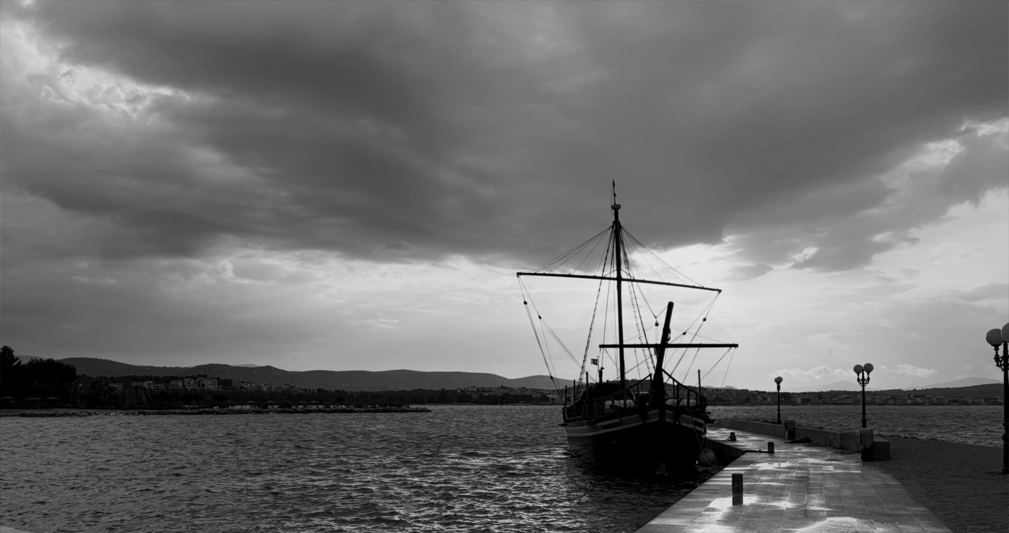 A ship moored at a dock in Šibenik under heavy clouds, in black and white