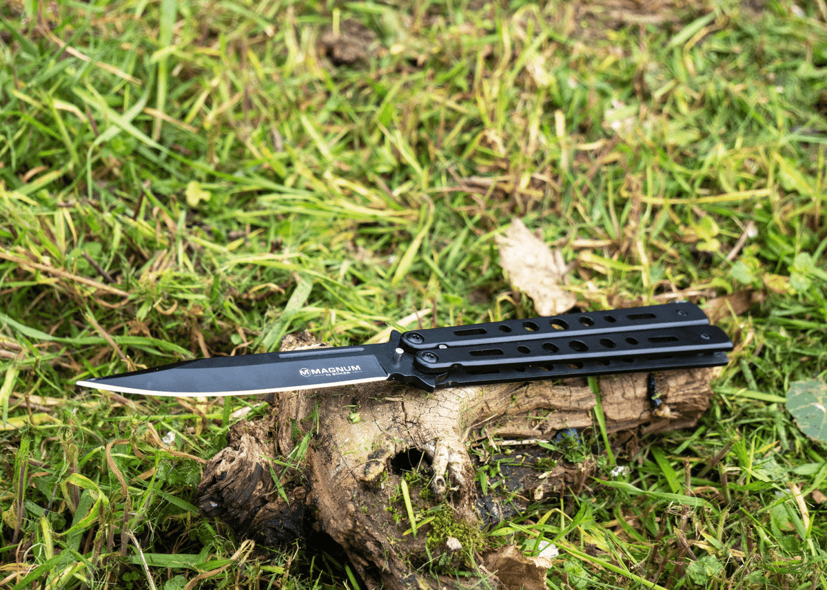 A black butterfly knife laying on a piece of wood in the grass