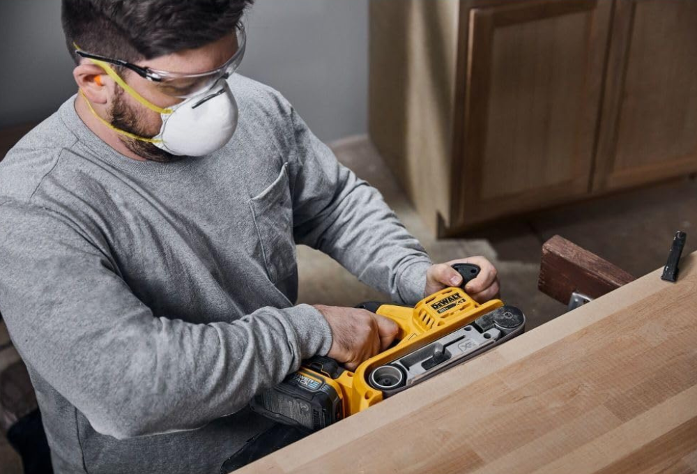A man sanding the edge of a counter top with a DeWalt belt sander, cordless