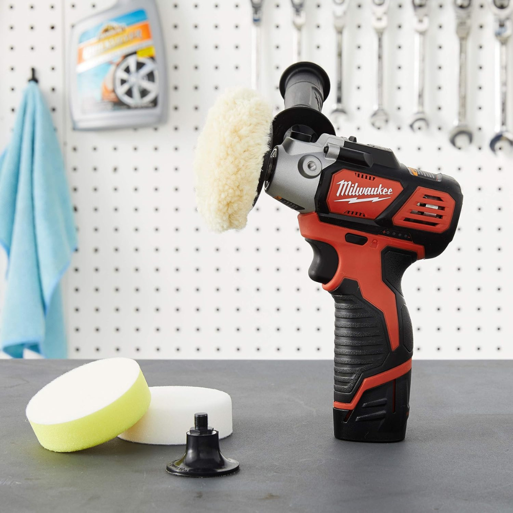 A mini buffer with pads on a work bench with a microfiber cloth hanging on peg board in the background.