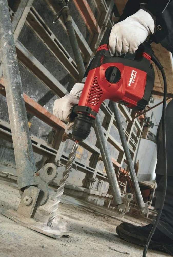 A man drilling a large hole in concrete for anchoring a wall structure.
