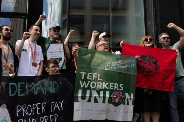 Photograph of a group of TEFL workers rallying outside EC English London raising their fists in the air while hodling signs and IWW banners.