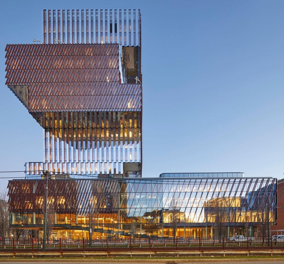 A glassy vertical tower, made up of irregularly stacked rectangular volumes, extends from a low, wide podium that is also glassed-in