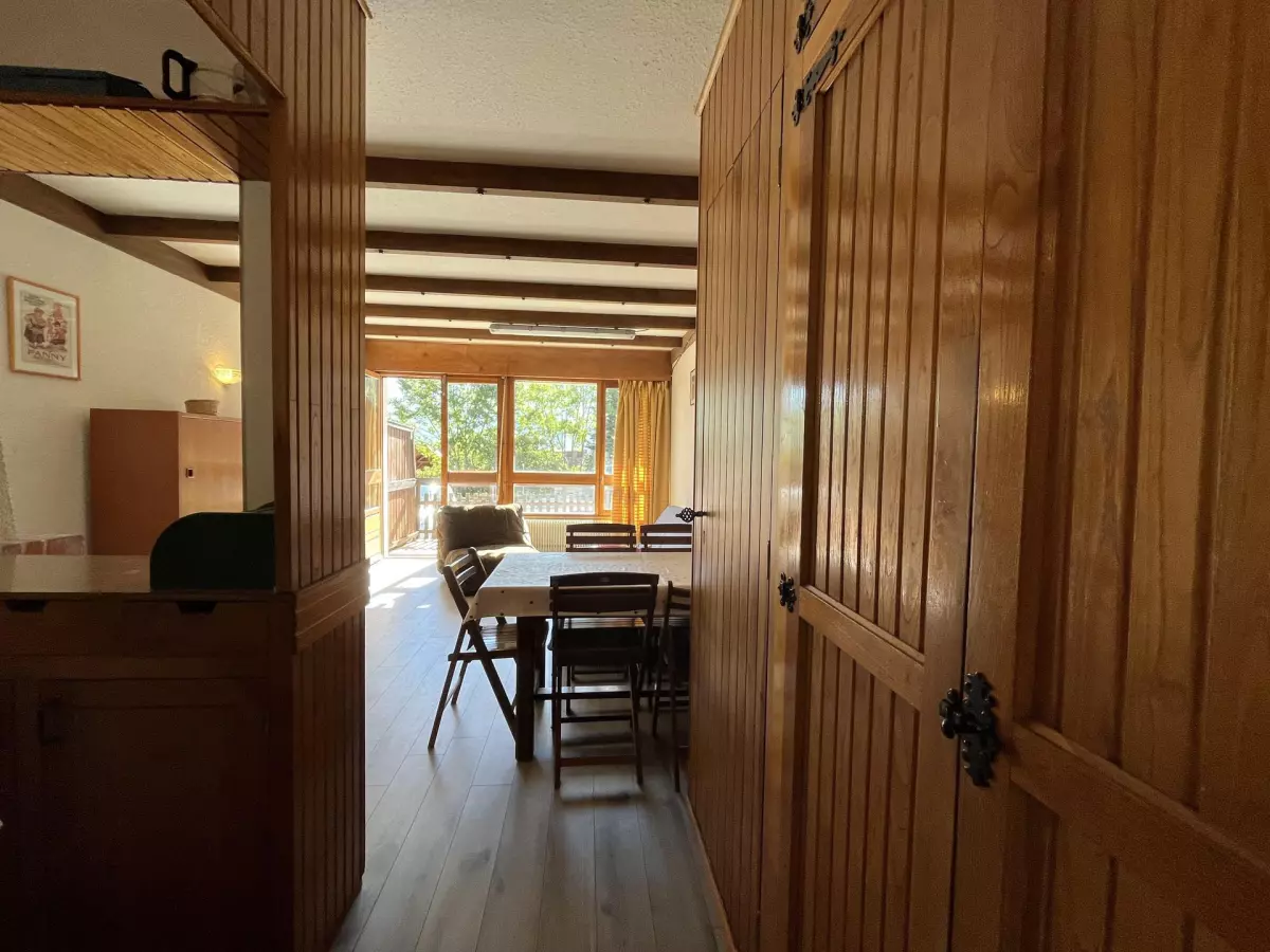 Entrée d’un appartement chaleureux avec mobilier en bois, ouvrant sur un séjour lumineux et une grande baie vitrée donnant sur la nature.