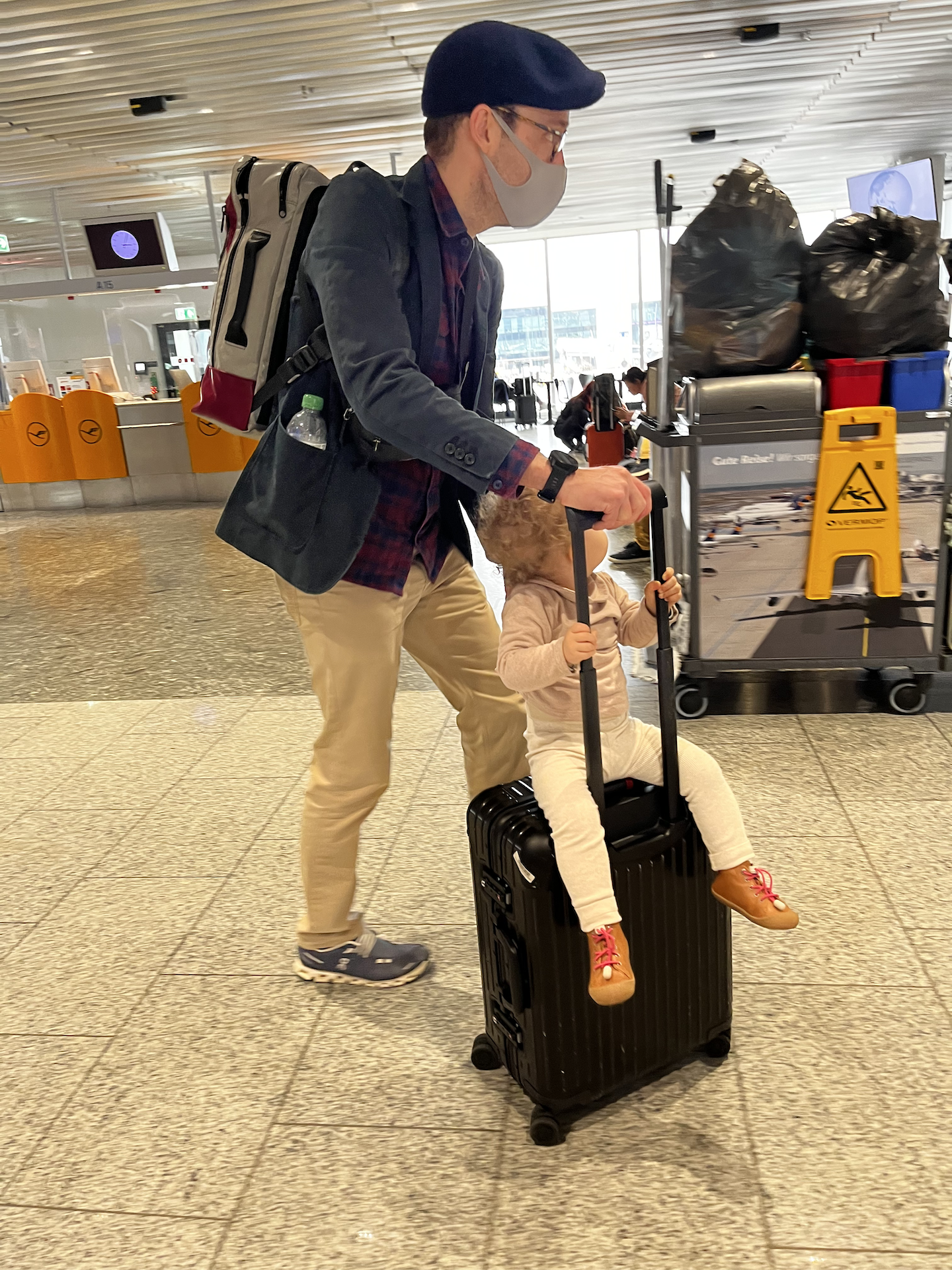 Child sitting on a suitcase being pushed by her father