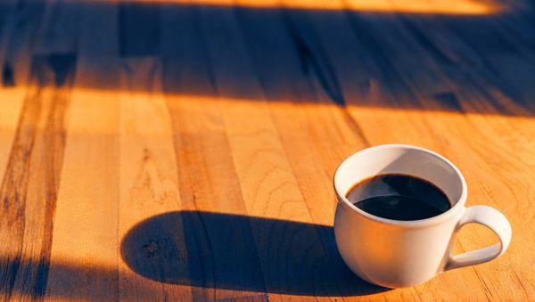 A white mug of coffee on a wooden table in morning sunlight