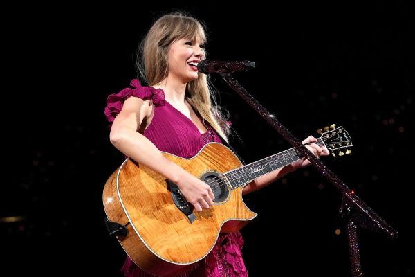 Taylor Swift sings while playing a brown guitar and wearing a fuchsia-purple ruffled dress.