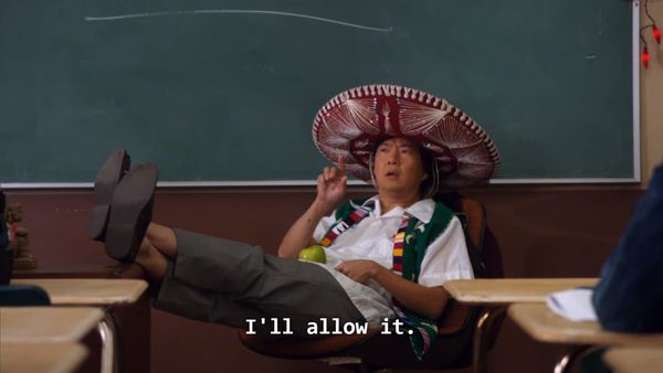 Ken Jeong relaxes at the head of a classroom, wearing a sombrero. He points upwardly while saying "I'll allow it."