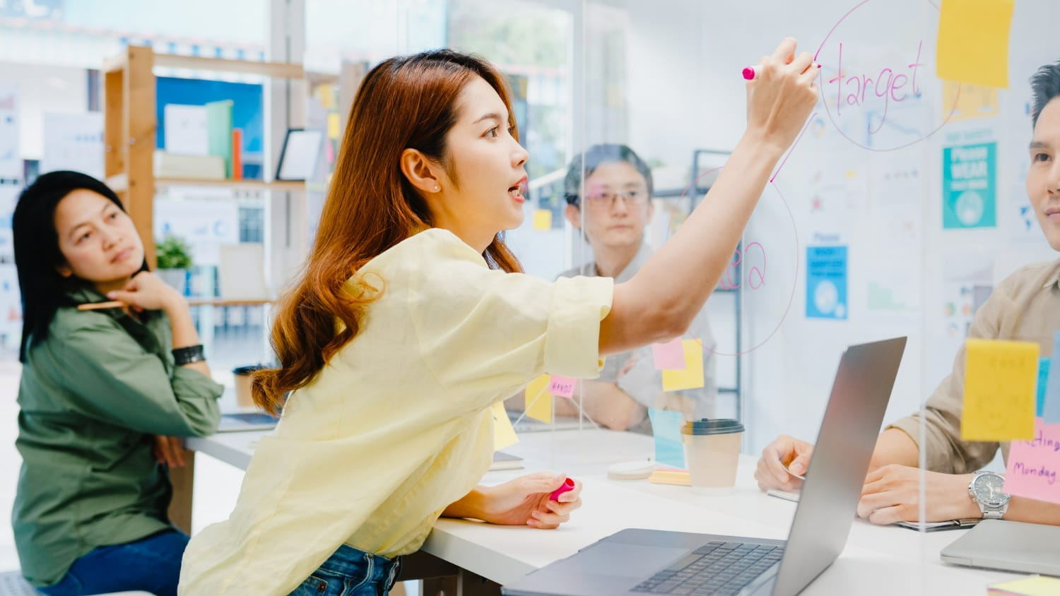 Asia businesspeople discussing business brainstorm meeting together share data and write on acrylic partition stand back in new normal office