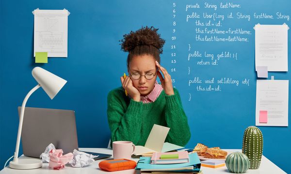 An image showing a female software developer under stress and codes written on a wall behind her.
