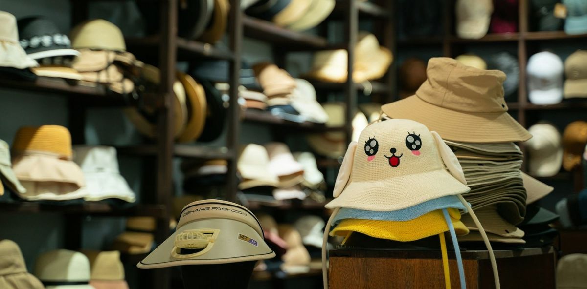 Display of various hats in a store, featuring a stack of cartoon-face bucket hats in the foreground