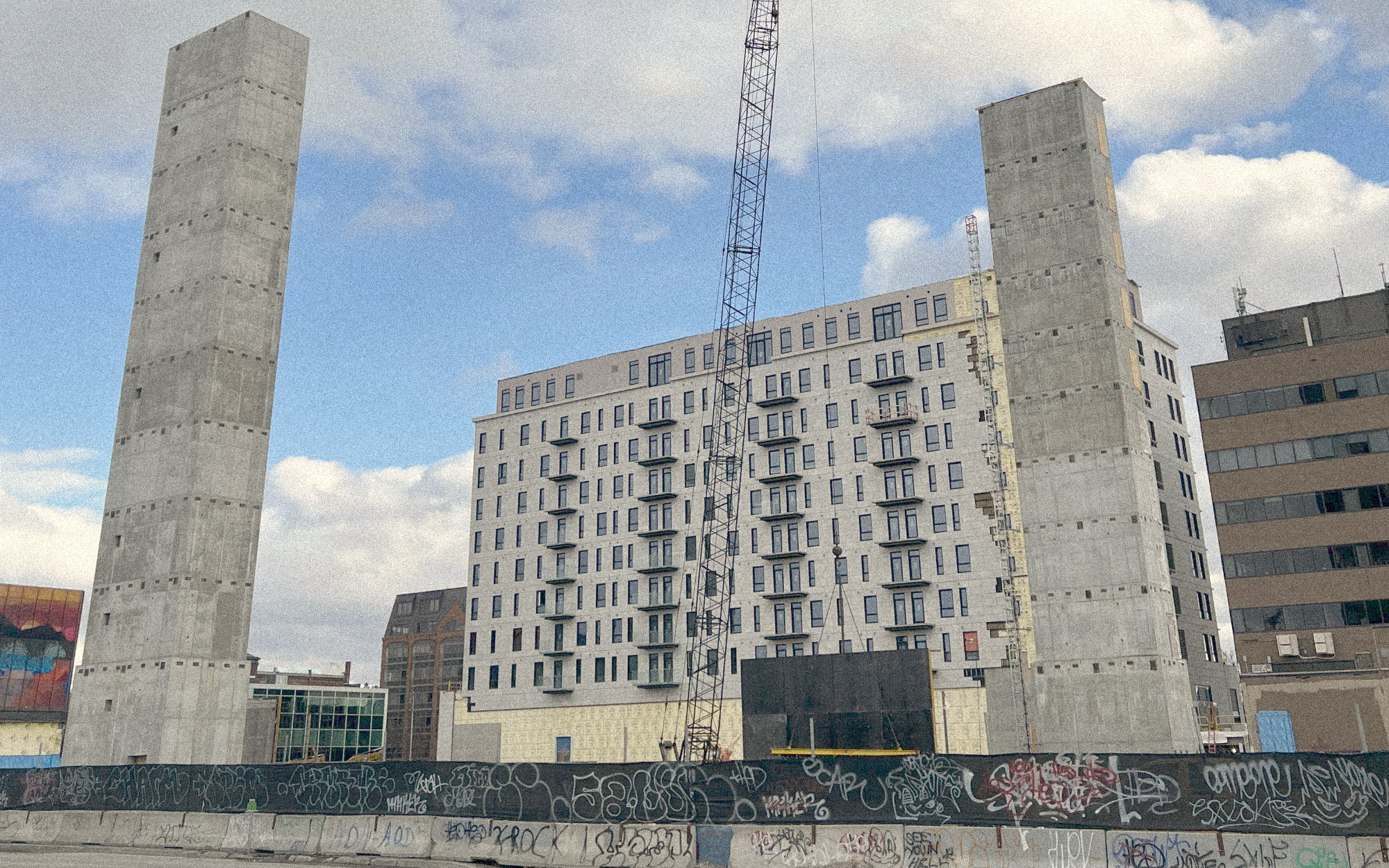 A large beige building rises, complete with crane. Two unconnected concrete elevator shafts frame the image.