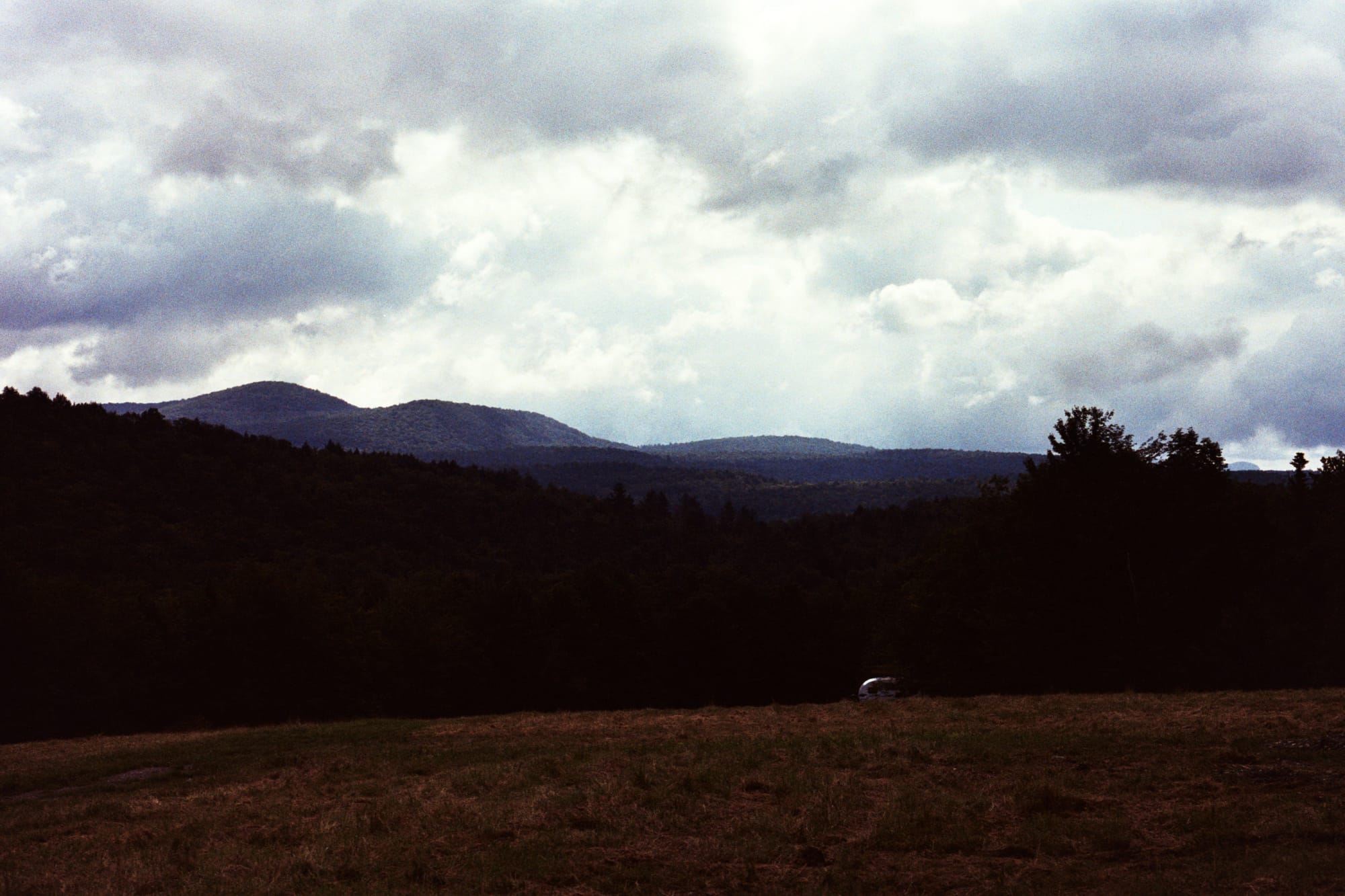 A color photograph of Vermont mountains. Foreground filled by a cut yellow field. 