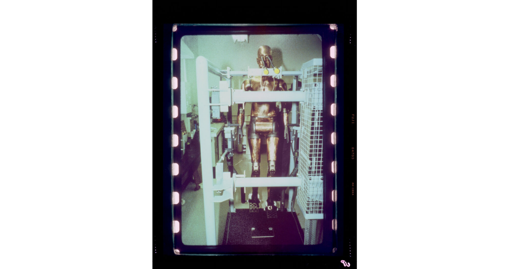 A gold robot stands within a cage. The image is a photograph of a film reel / color film negative.