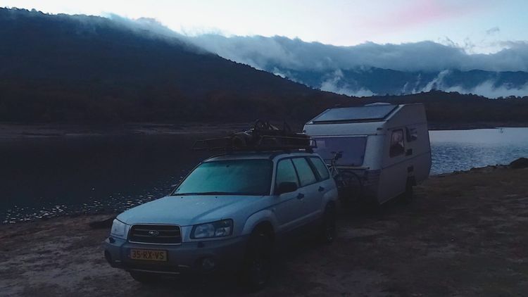 Car and solar-powered caravan by a lake
