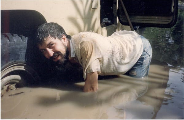 A man on his hands and knees in a mudhole by a car